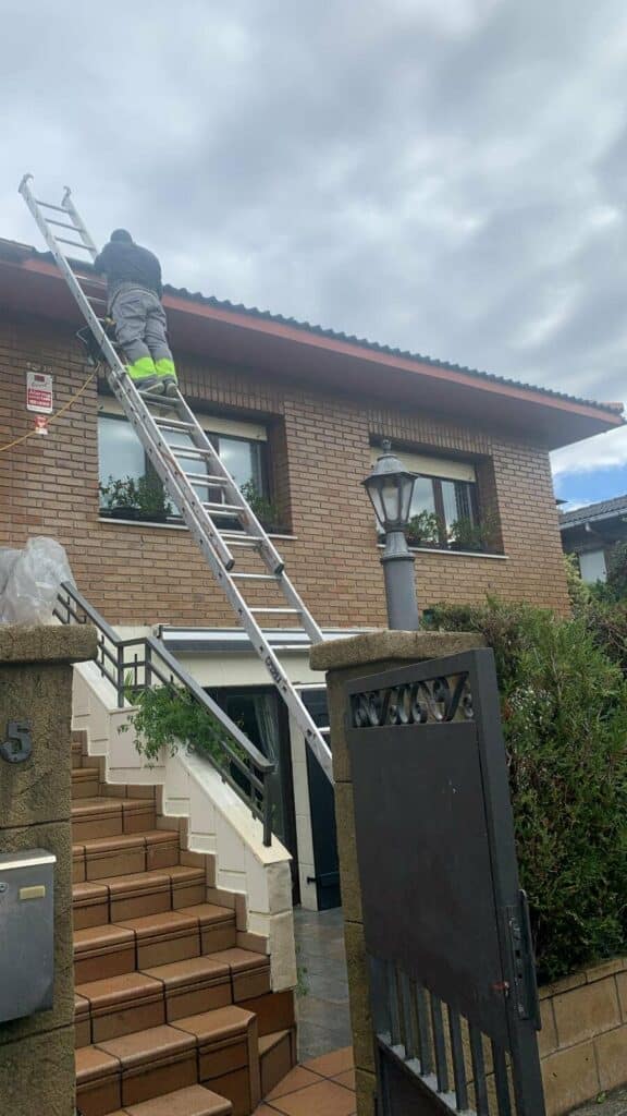 Escalera apoyada en una fachada de ladrillo para revisar el alero