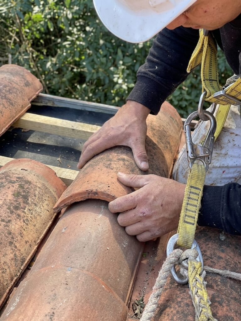 Detalle de manos de un tejero encajando una teja curva cerámica en cubierta en San Sebastián